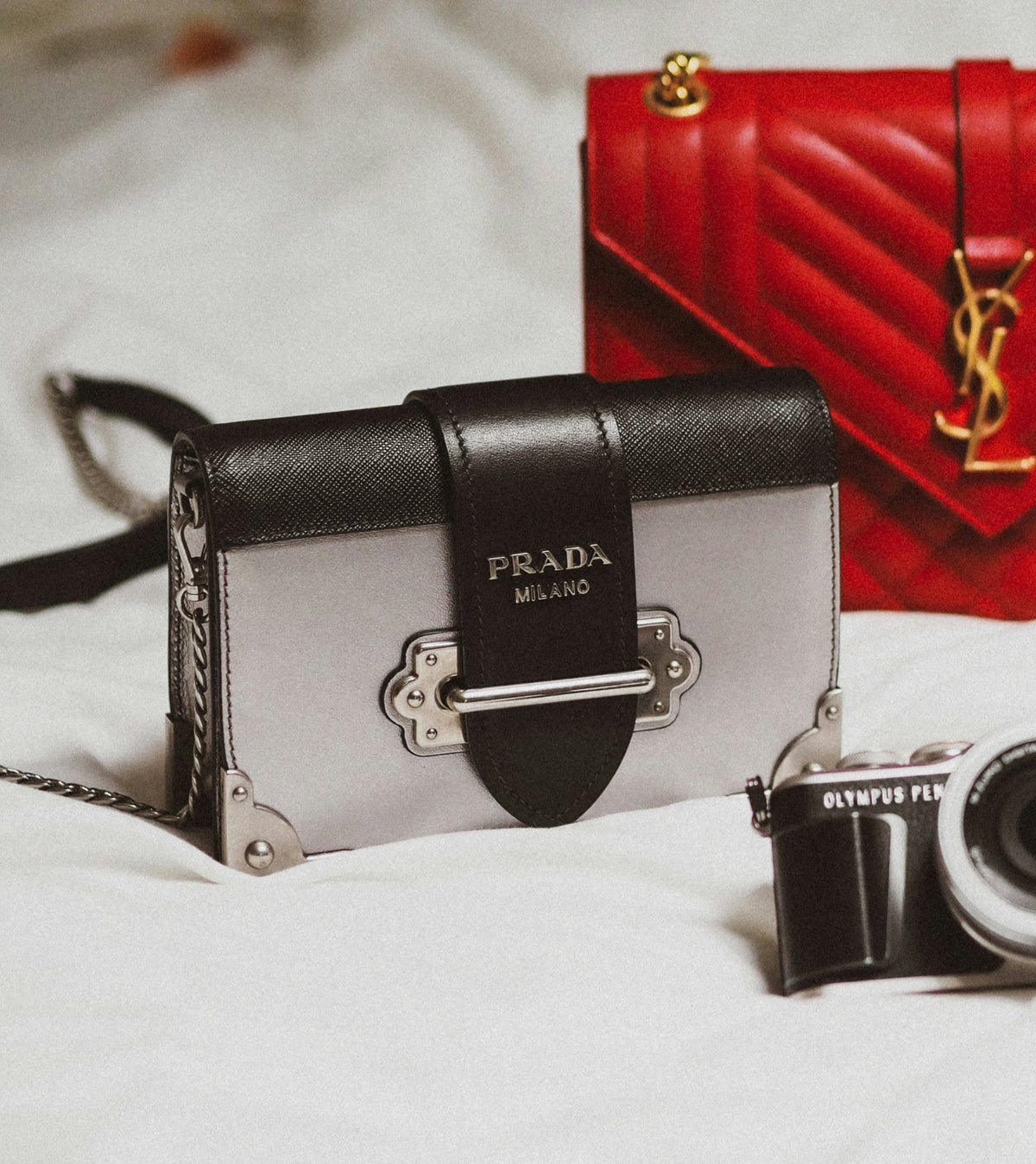 Prada Cahier and a red YSL bag on a bed